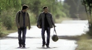 Sam and Dean walk along a deserted road.